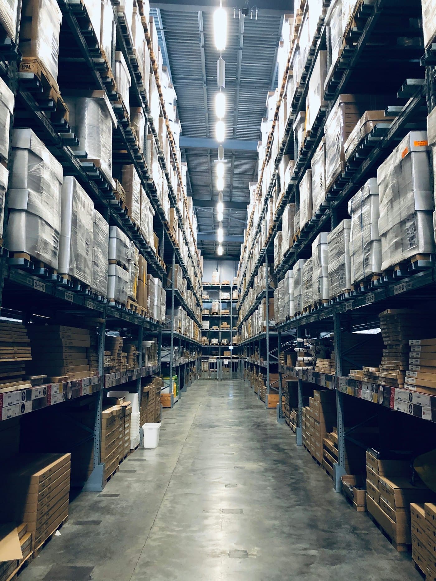 A long warehouse aisle between tall shelving of boxed inventory